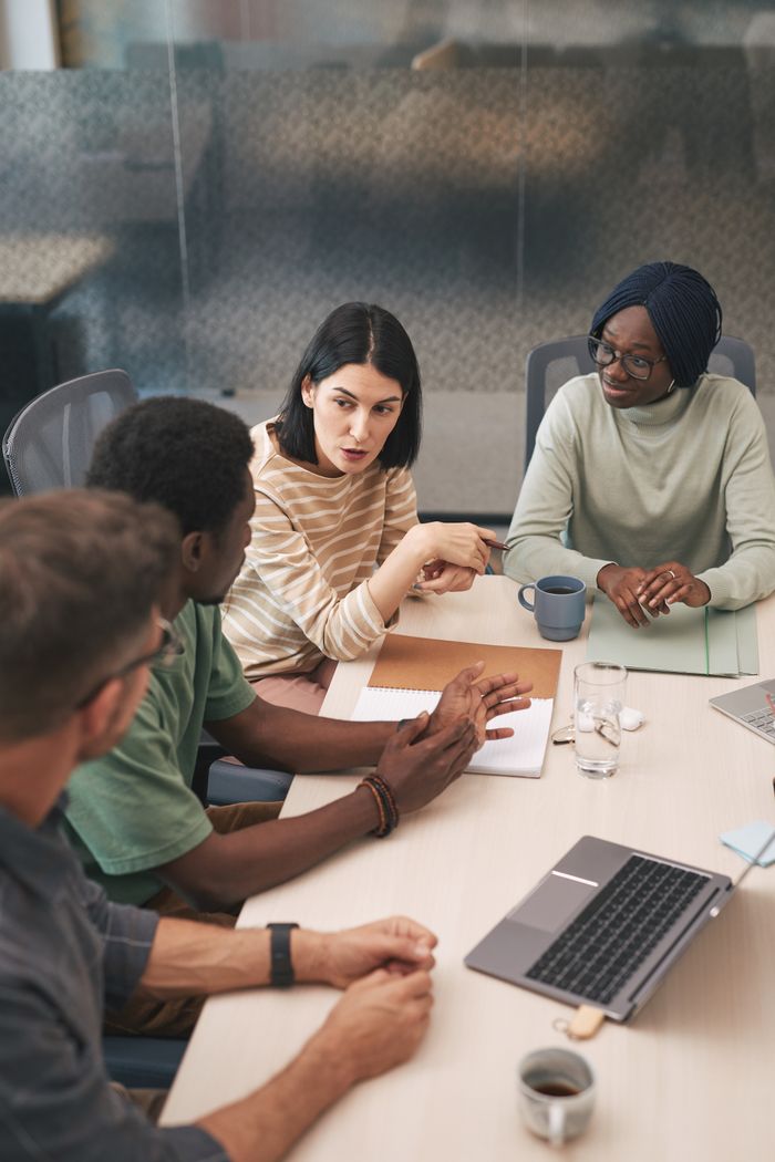 A diverse group of colleagues having an active meeting in a modern office setting with a laptop.